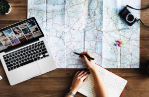 photo of a person planning a trip using a laptop and a map